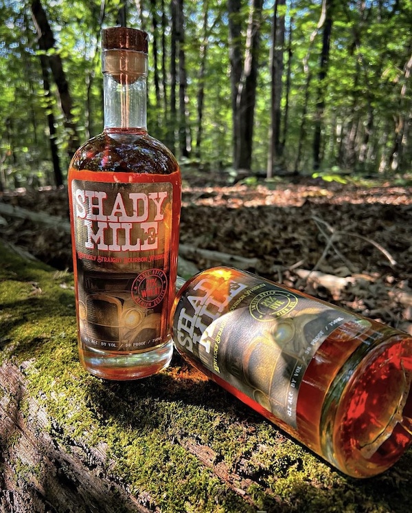 two bottles of shady mile bourbon in forest